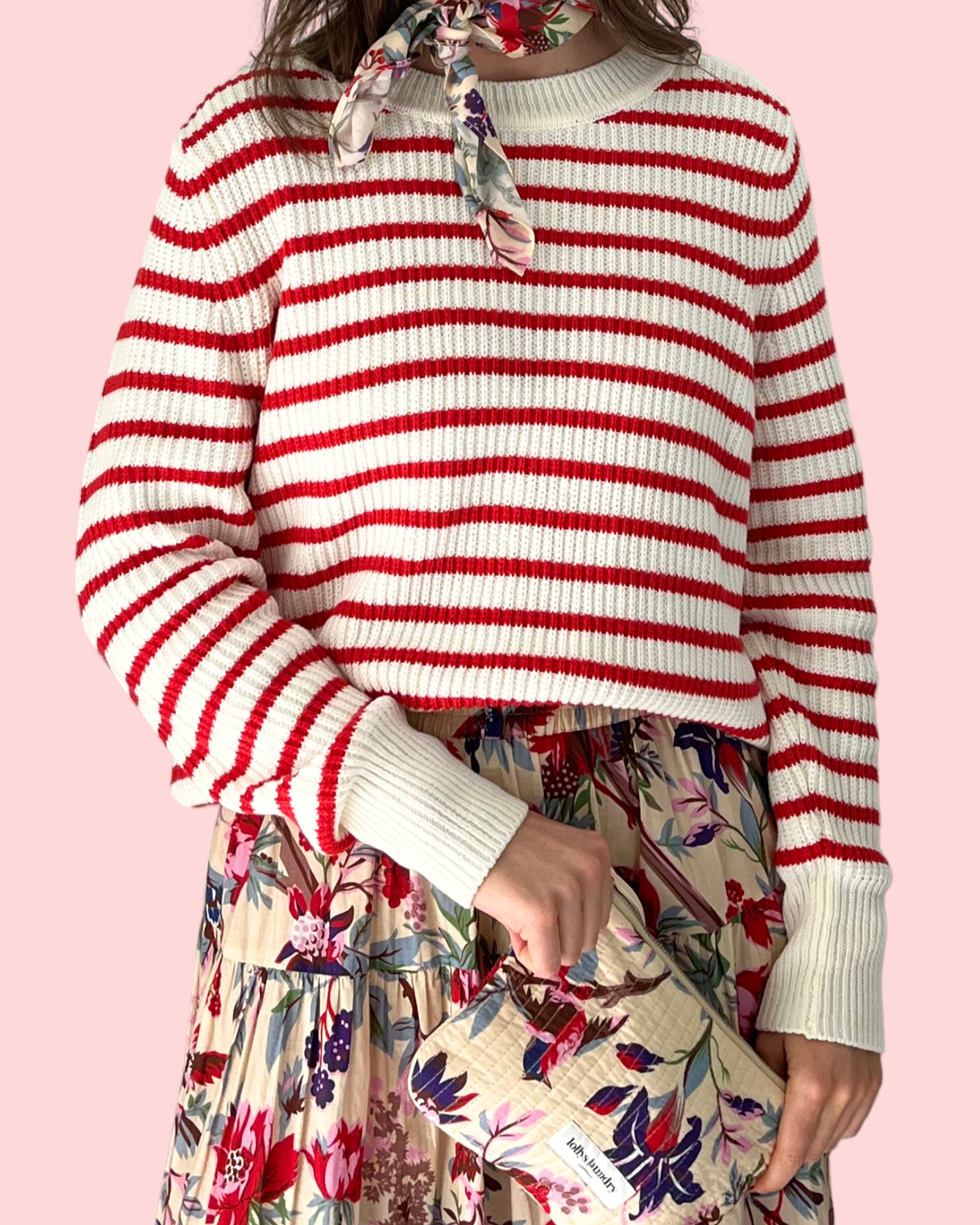 Person wearing a red and white striped sweater with a floral skirt and bag on a pink background