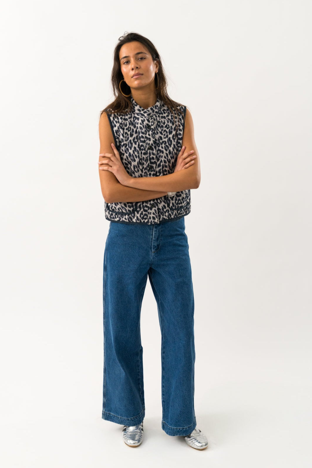 Person wearing a sleeveless patterned top and blue jeans on a white background