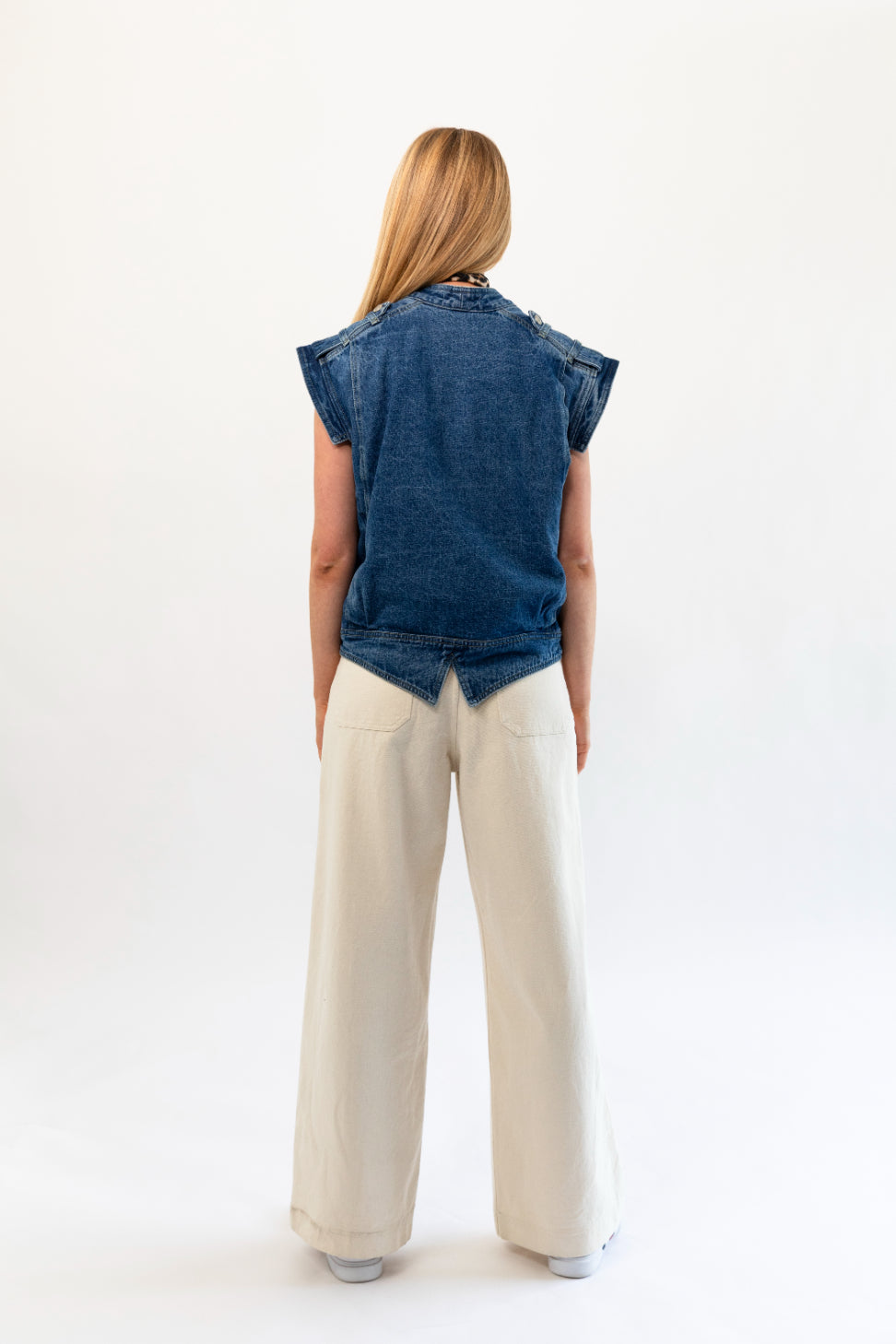 Woman wearing a denim vest and beige pants on a white background