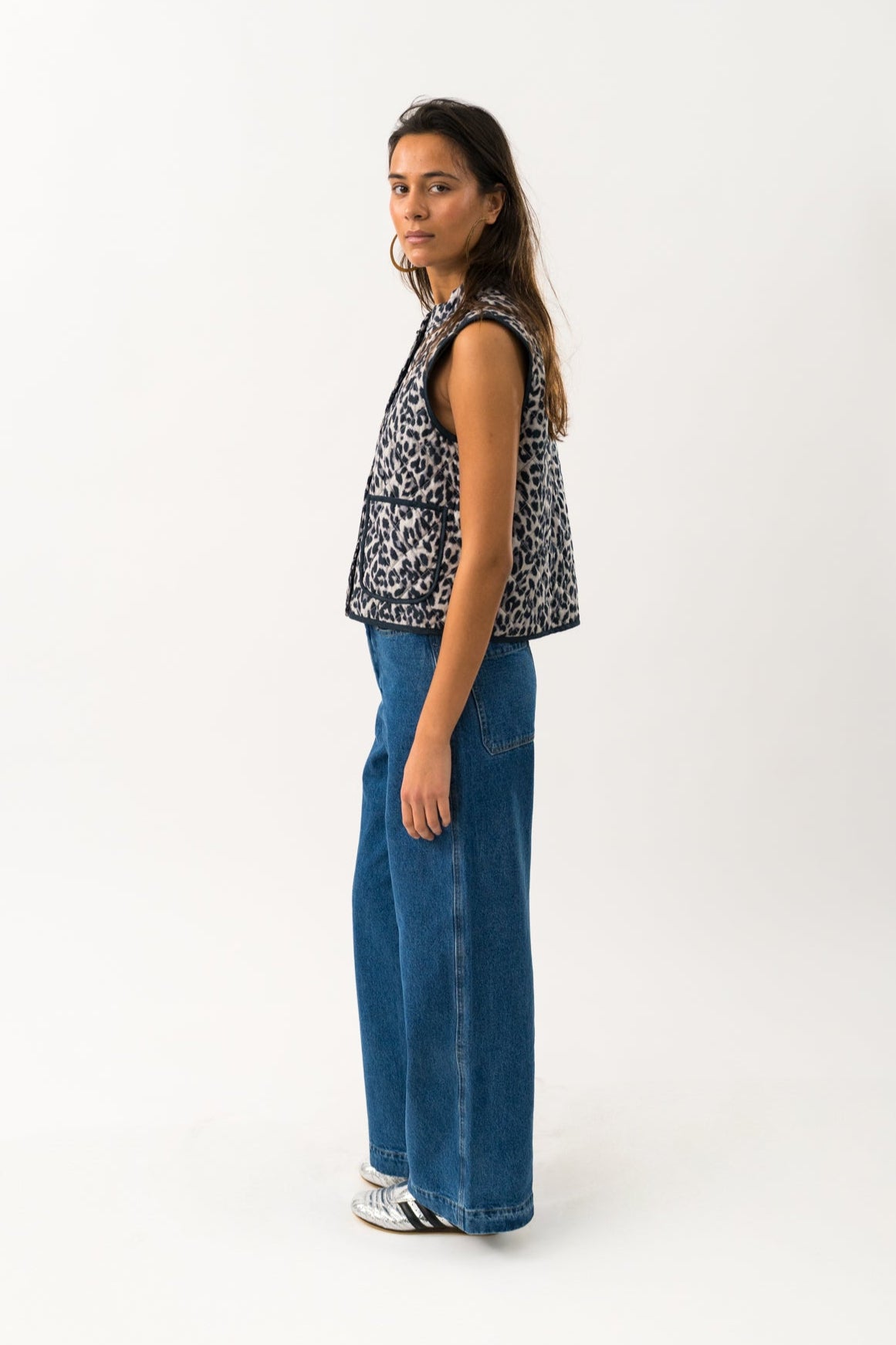 Woman wearing a patterned sleeveless top and blue jeans on a white background