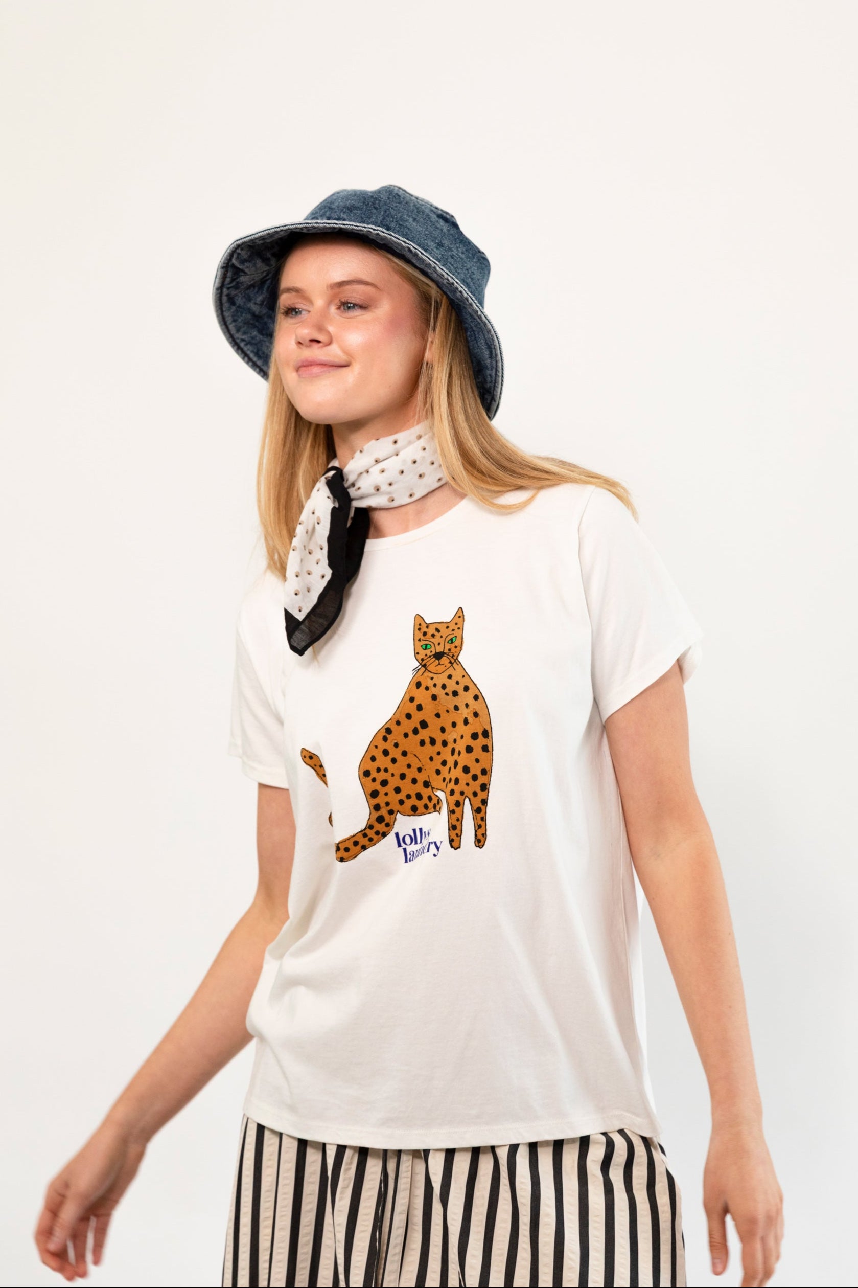 Woman wearing a white t-shirt with a cheetah design, a denim hat, and a black and white scarf on a white background